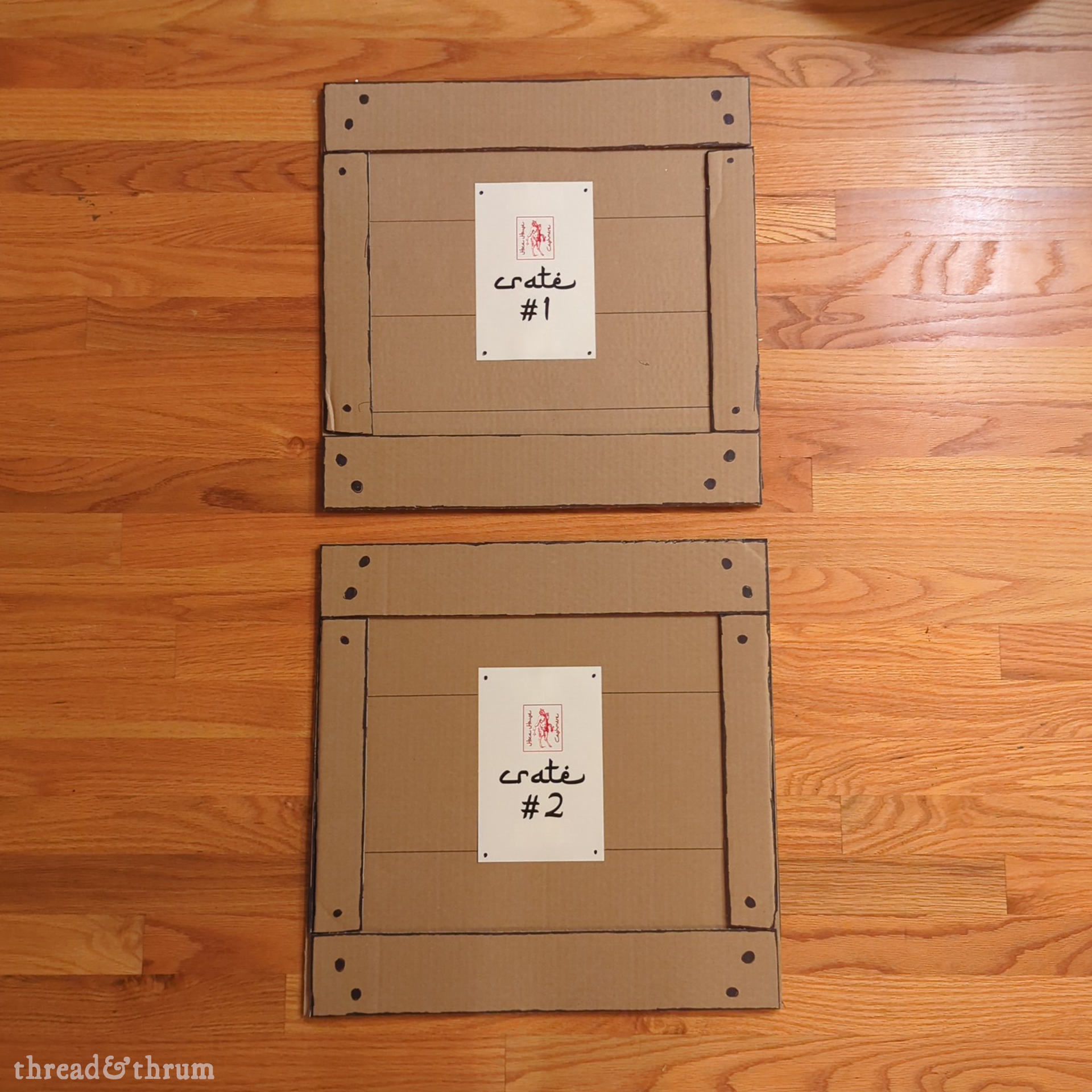 Two prop pieces that look like the front of big wooden shipping crates, made from cardboard, with signs attached reading "Hoca House Cashmere" crates 1 and 2, laid out on a wood floor